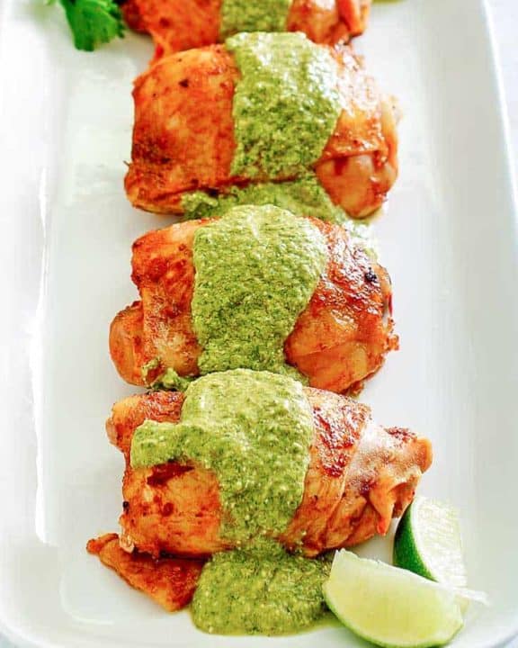 四个秘鲁鸡大腿用在盛肉盘的绿色调味汁